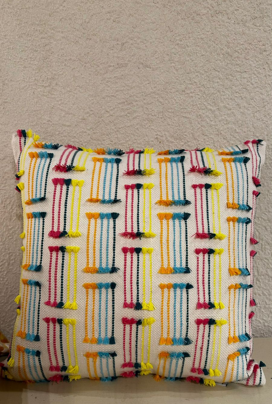 Multicolored woven pillow with tassels on a neutral background